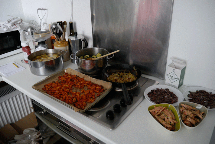 kitchen counter and stove with trays, pots, and bowls of food atop