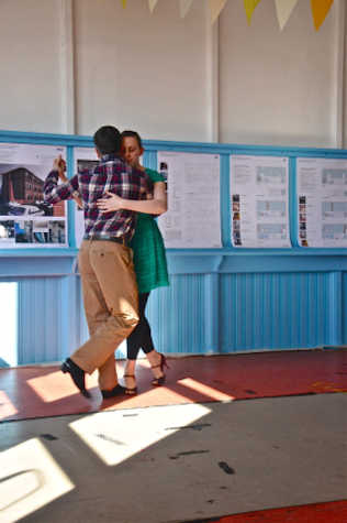 Two people, a man and a woman are dancing together. The room has bright walls and some streamers attached to the ceiling.