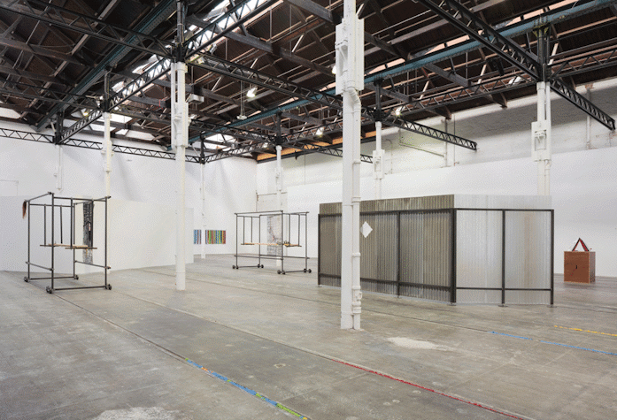 A big room with white walls and grey floors. White columns and black trolleys as well as the metal structures.