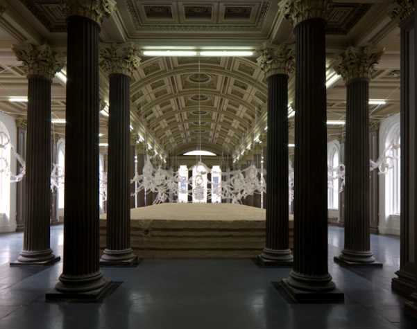 gallery installation, large pillars in foreground with view of sculptural works in background