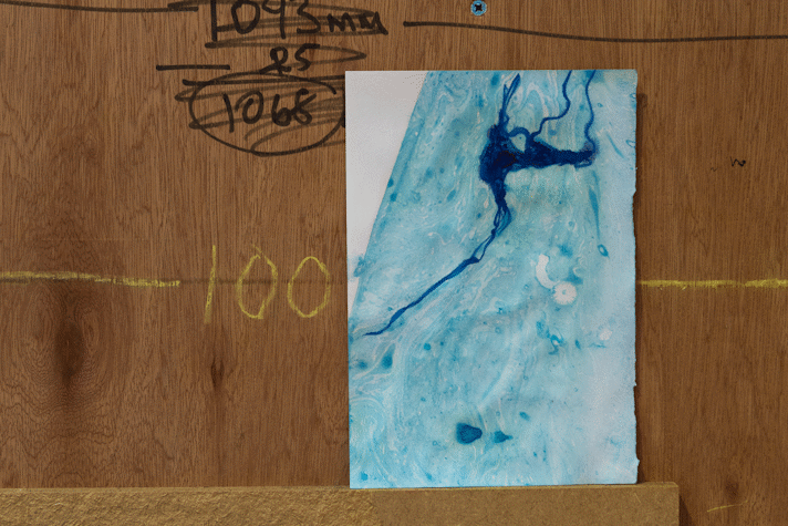 an A5 abstract ink painting sits on a ply wood ledge