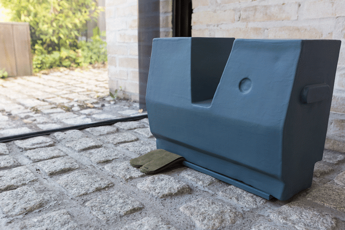 abstract teal sculpture with khaki leather trapped under it, sits on a cobble stone floor