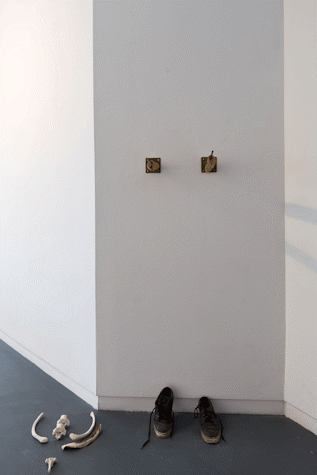 sculptural assemblage in the corner of a gallery. There are trainers, a pile of bones.