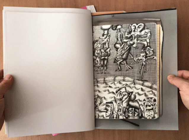 hands hold open an A5 booklet, the right page shows a scan of a sketchbook page with black ink drawing of cartoon characters