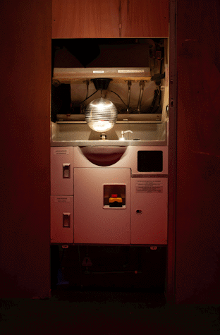 Image of Jenkin van Zyl's installation at Tramway. An aeroplane sink unit has a disco ball hanging over it. There is red overhead lighting.